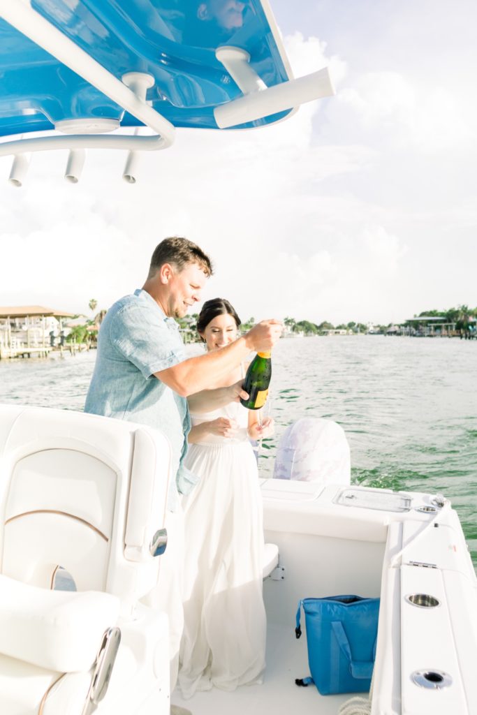 Groom pop a champagne on the boat for their backyard wedding day.