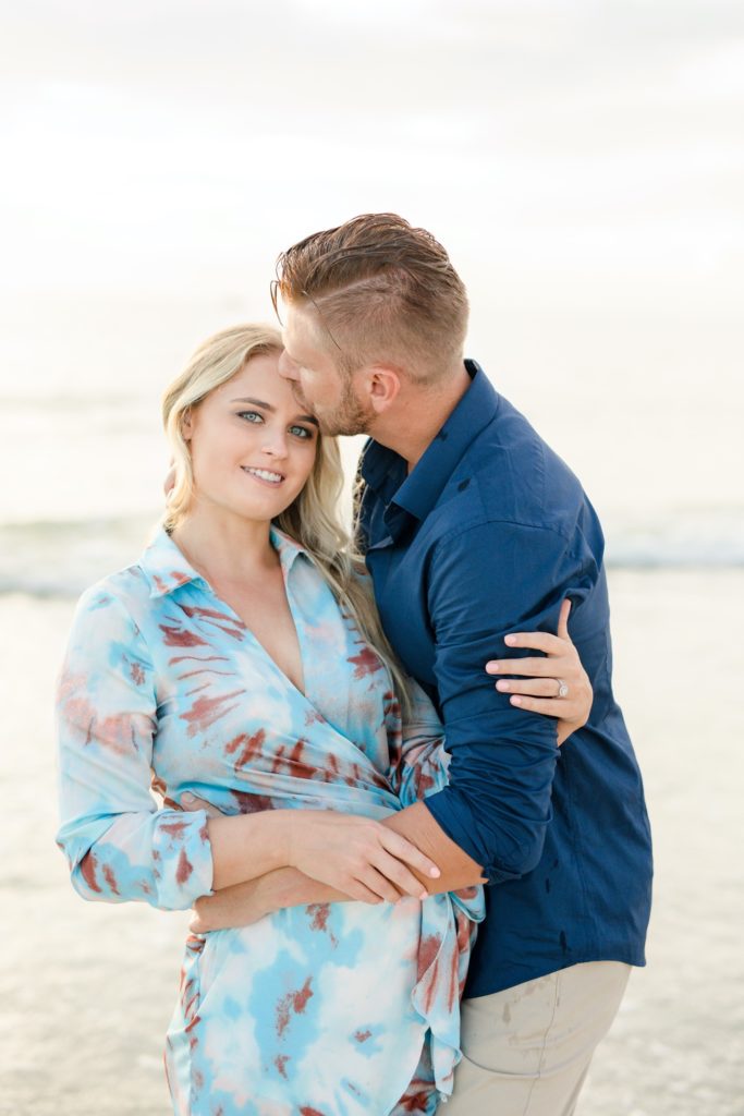He kissing her forehead on the sunset beach engagement session
