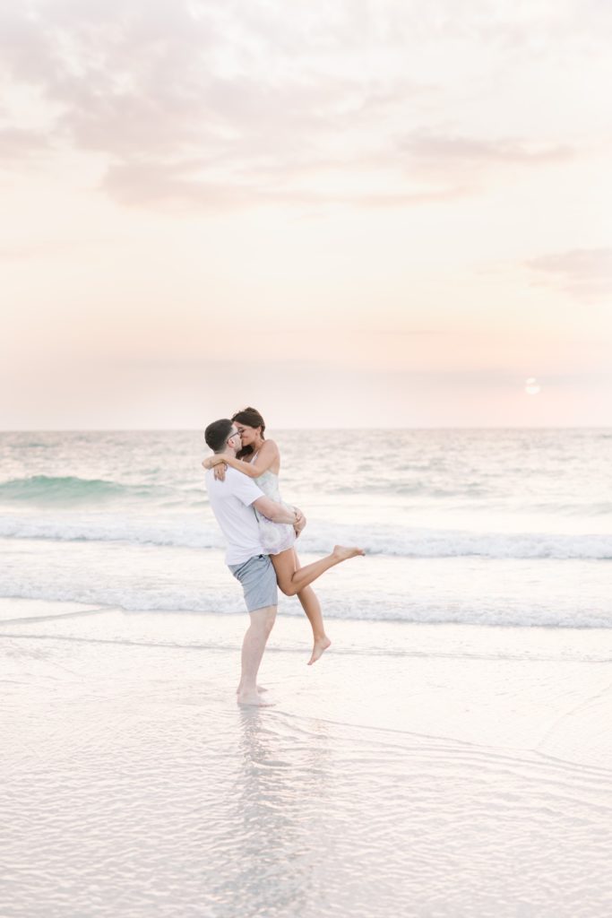 Couple is kissing and twirling on their fall engagement session on the beach