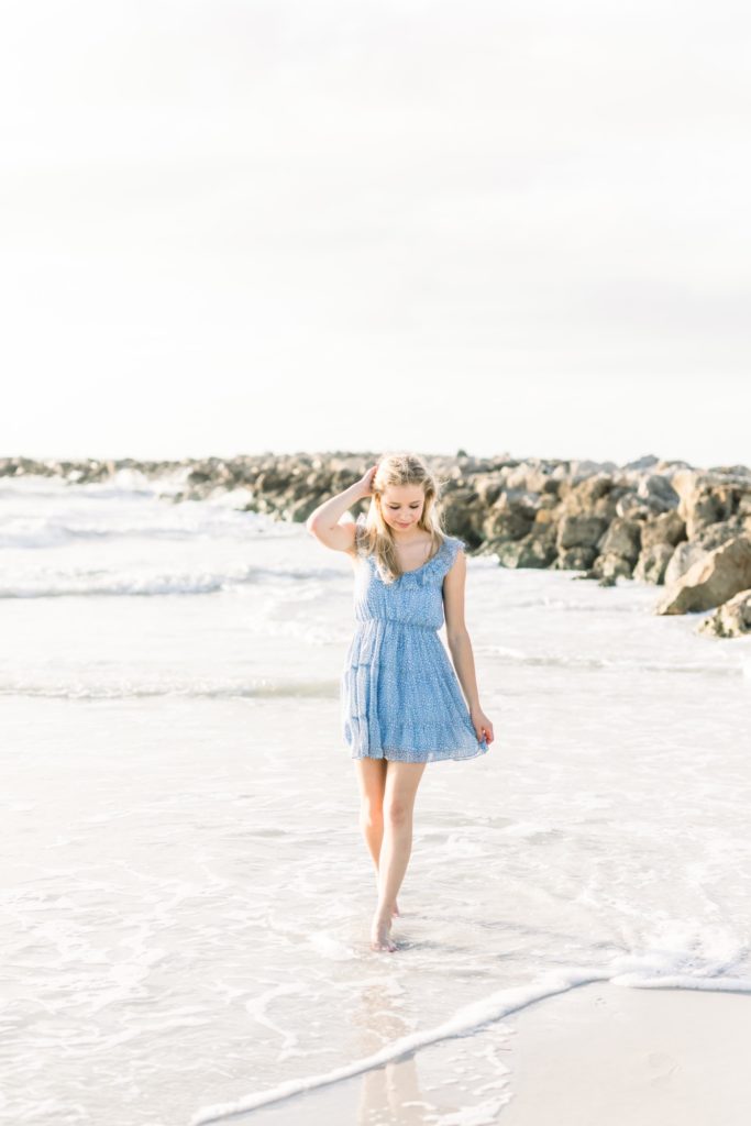 Senior is walking and holding the dress while walking on the beach.