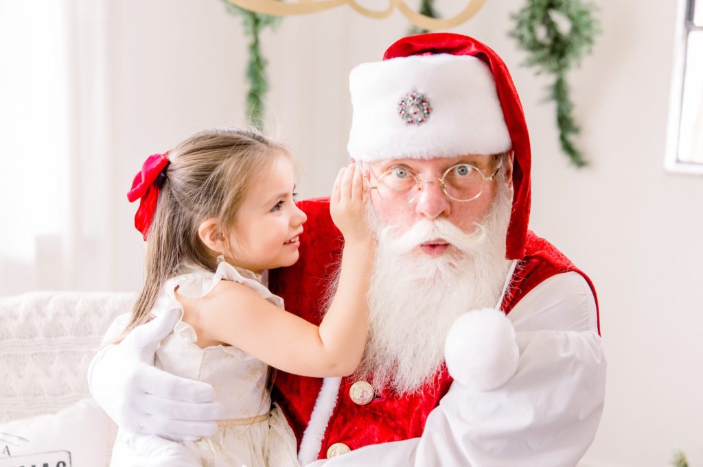 A girl whisper in Santa ear at Santa Mini Sessions.