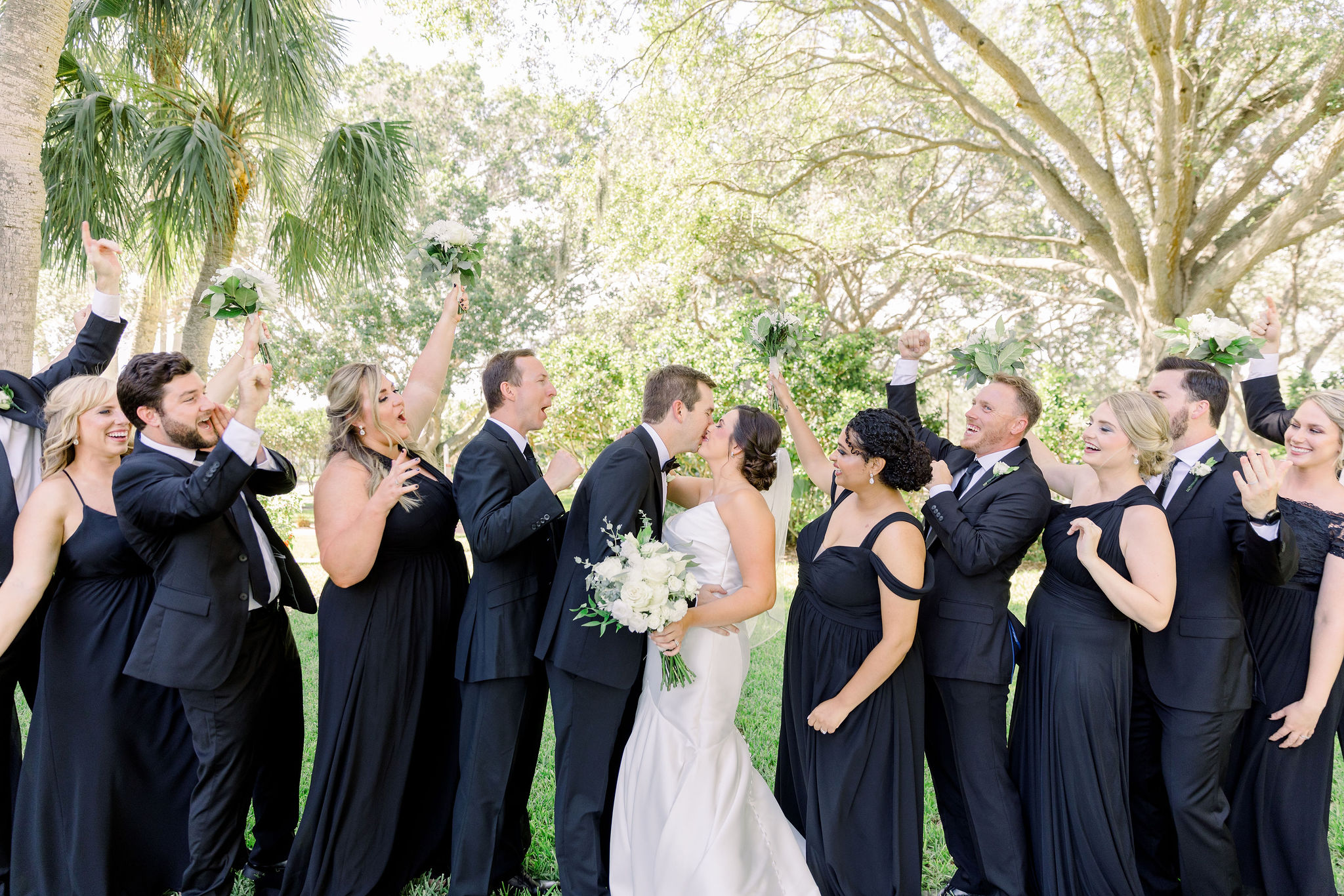 A bridal party cheer as the bride and groom kiss on golf greens in Manatee County, Florida by Jommy Photography. A high-end wedding photographer in the Manatee County area. Fun wedding portraits with the bridal party.
