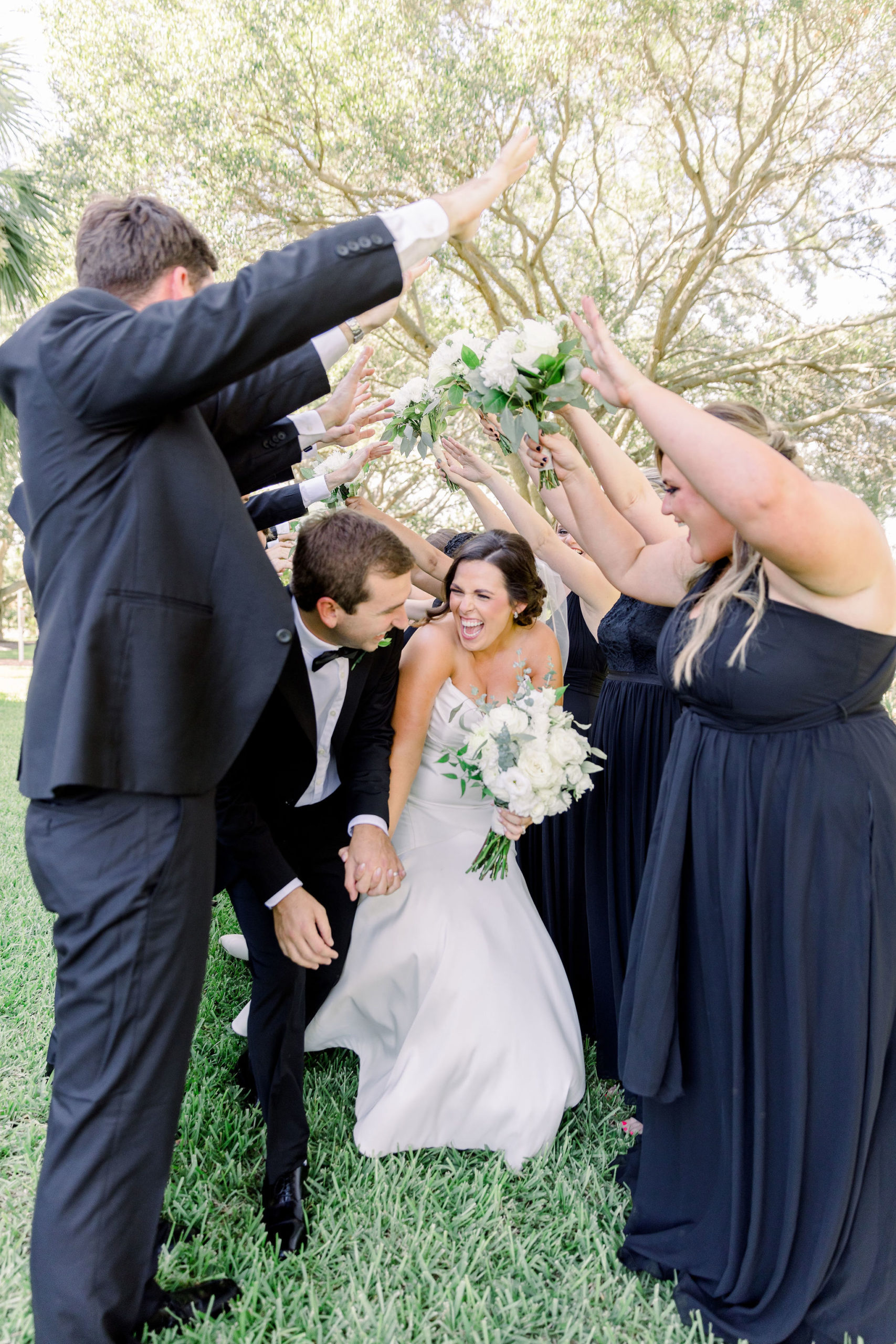 The groomsmen and bridesmaids make an arch pathway with their arms so the bride and groom can run through it by Jommy Photography. Florida wedding photographer captures a bride party making a archway for the newly wed couple.
