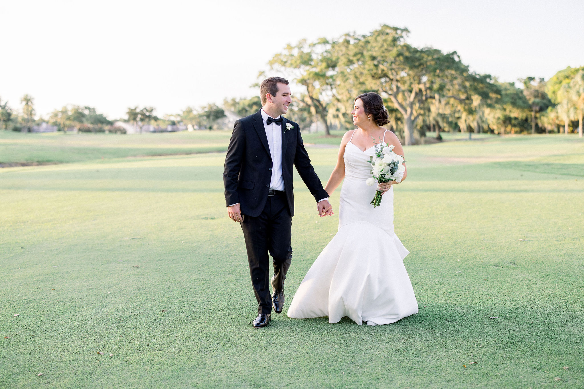 At the Bradenton, Florida IMG Golf Course a newlywed couple hold hands and smile at one another captured by Jommy Photography. Professional wedding photographer captures a bride and groom on their happy day.
