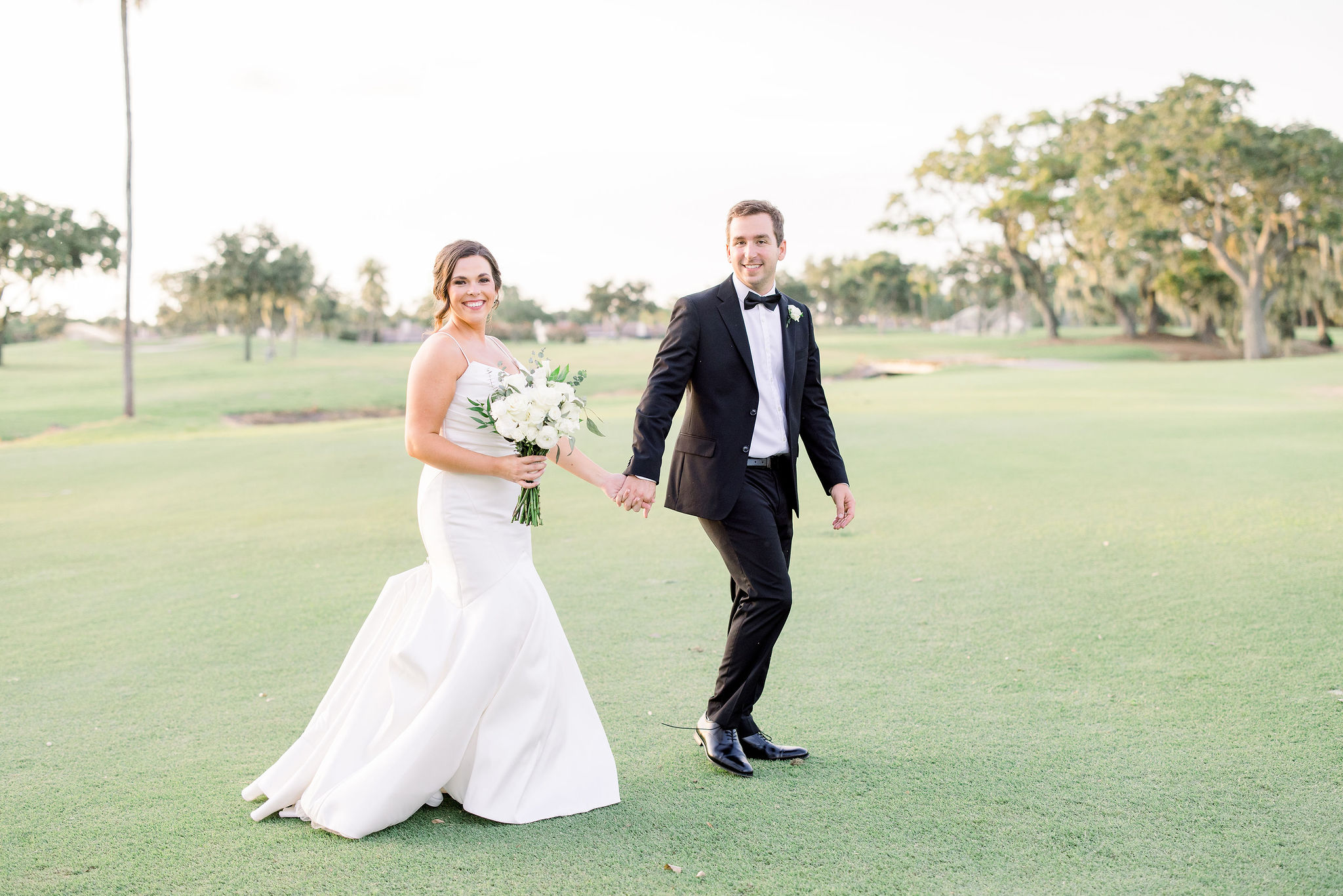 Bride and groom holding hands and walking on the green of the golf course in Bradenton, Florida on their wedding day captured by Jommy Photography. Manatee County, Florida outdoor and indoor wedding locations.
