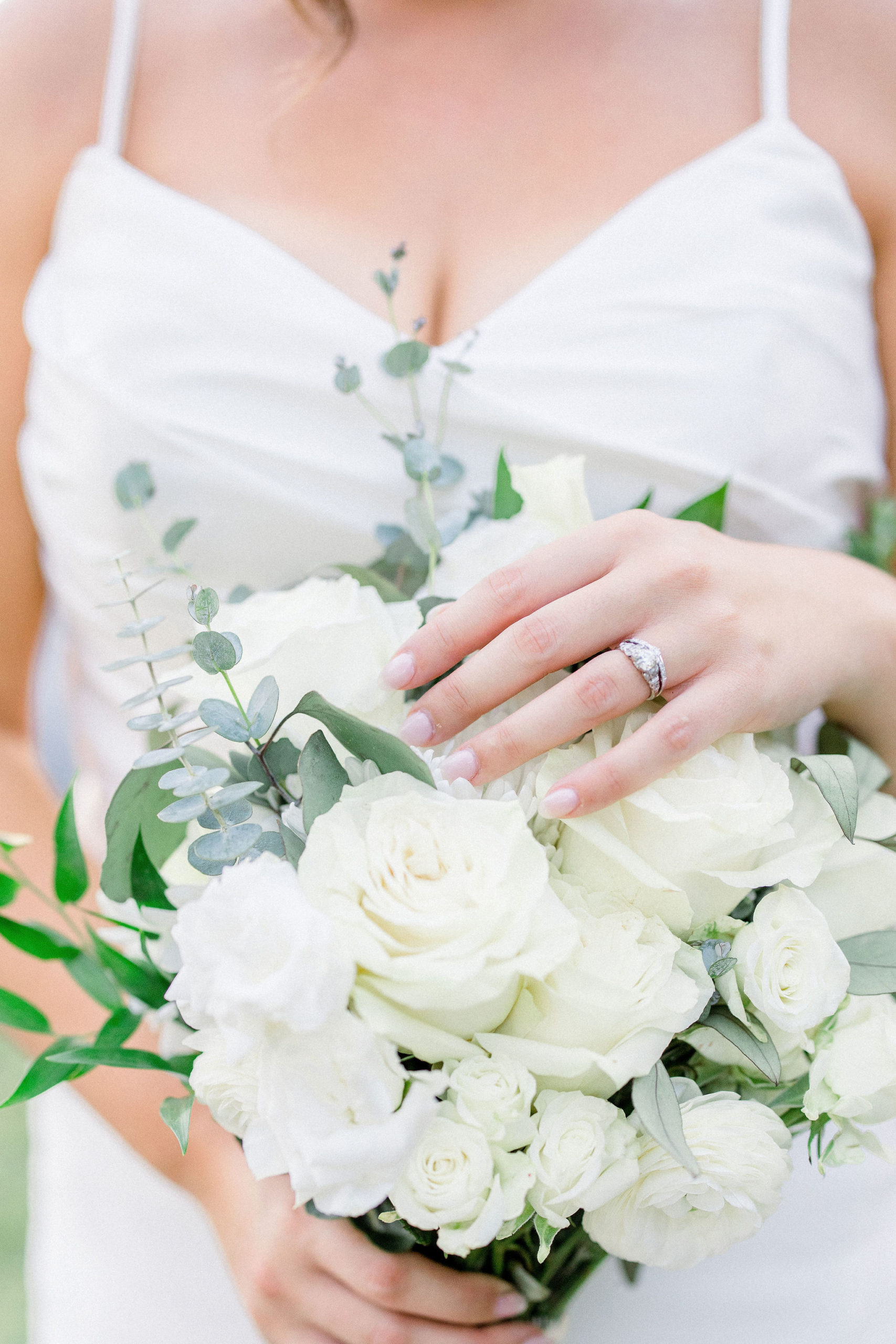 Close up of a white rose bridal bouquet and a silver vintage wedding ring on the brides finger by Jommy Photography. Silver wedding ring with a dainty silver diamond bridal band on a white floral bouqet.
