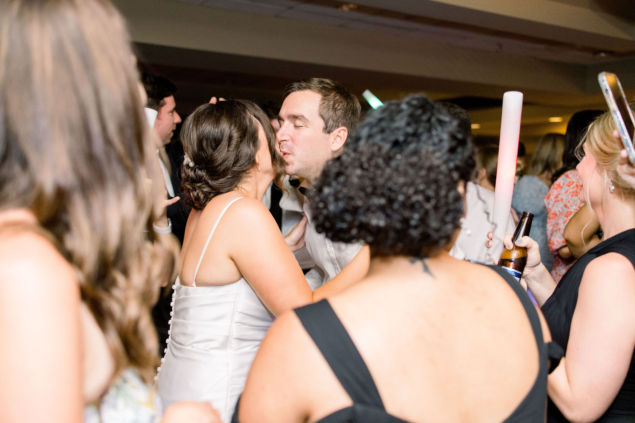 A bride and groom kiss on the dance floor as the guests party around them at the IMG Golf Course in Bradenton, Florida by Jommy Photography. Jommy Photography captures a bride and groom kissing while dancing at the reception.
