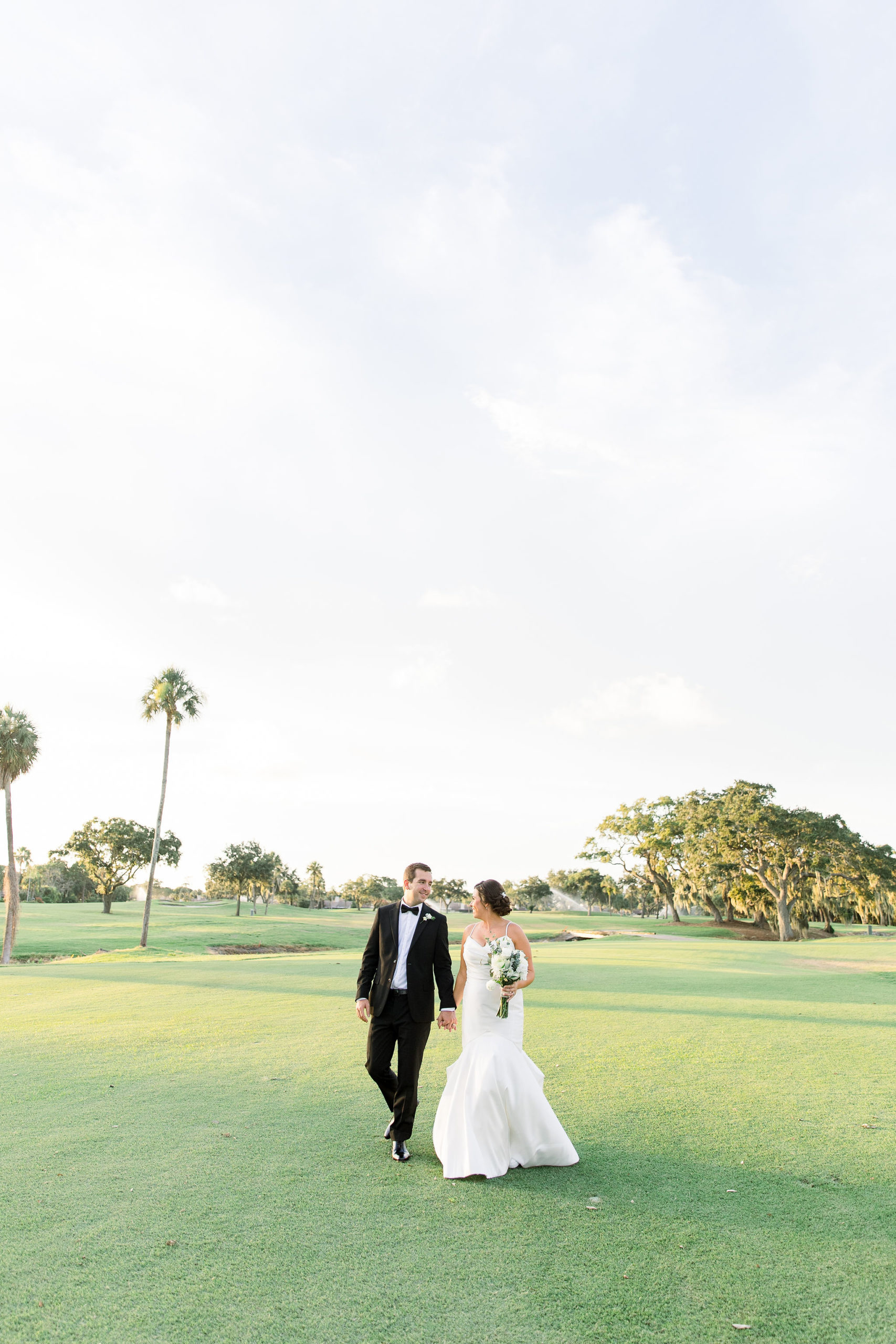 A bride and groom smile at one another while holding hands on sunny day at the IMG Golf Course in Bradenton, Florida by Jommy Photography. Florida Golf Course wedding captured by wedding photographer Jommy Photography.
