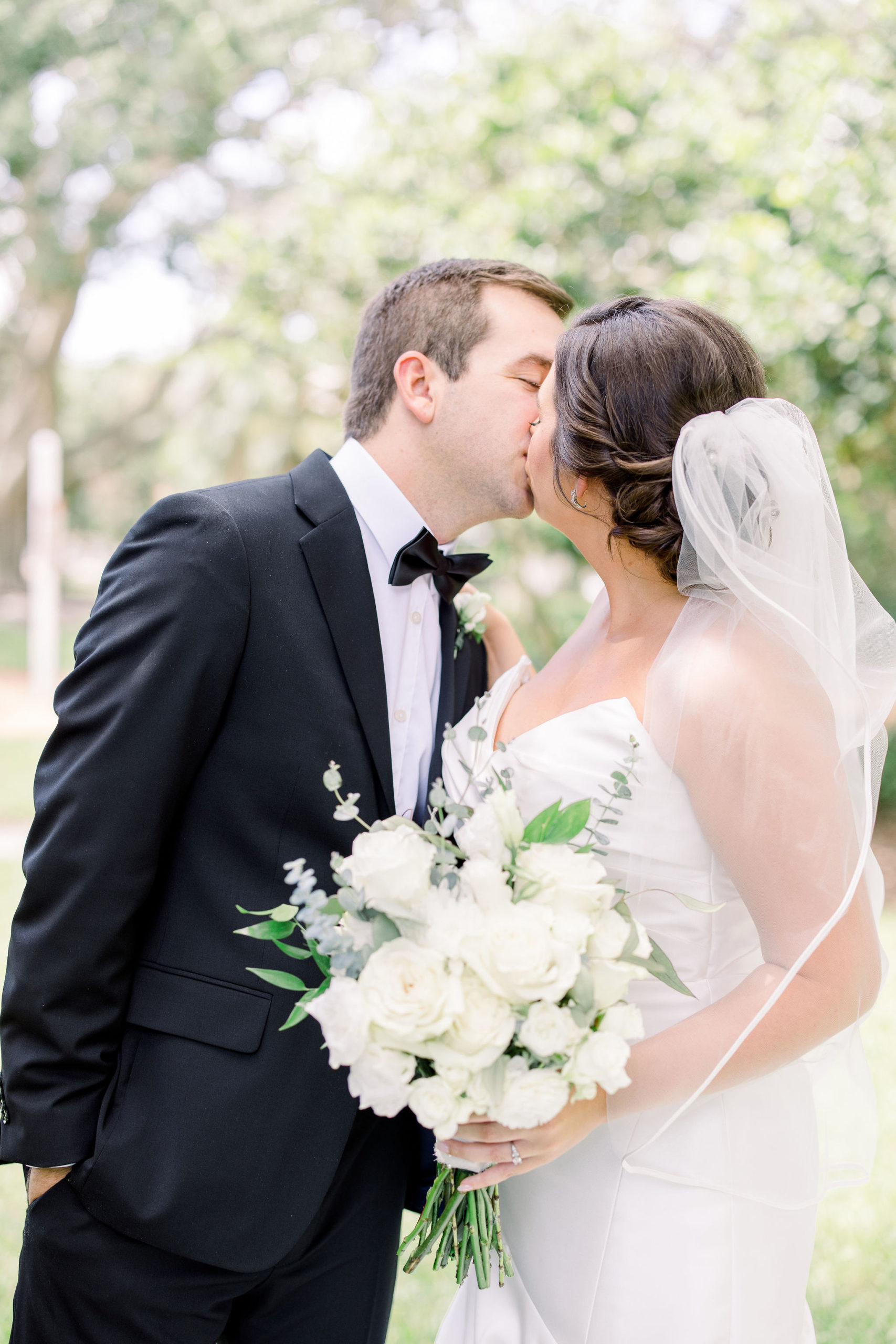 Wedding Photographer Jommy Photography captures a bride and groom kissing on their big day at a golf course. Bride with brown hair in an updo and veil kisses her new husband passionately on her wedding day.
