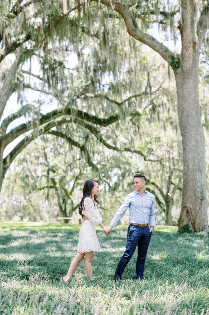 The husband leads his wife along under mossy oak trees by Jommy Photography. Florida couples #JommyPhotography #JommyCouples #FloridaCouplesPhotography #ProfessionalPhotographer #beachphotographer #coupoles #romanticcouples