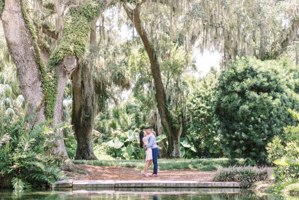 In a tropical location, a man and woman kiss under palm trees next to the water's edge by Jommy Photography. FL Photog #JommyPhotography #JommyCouples #FloridaCouplesPhotography #ProfessionalPhotographer #beachphotographer #couples #romanticcouples
