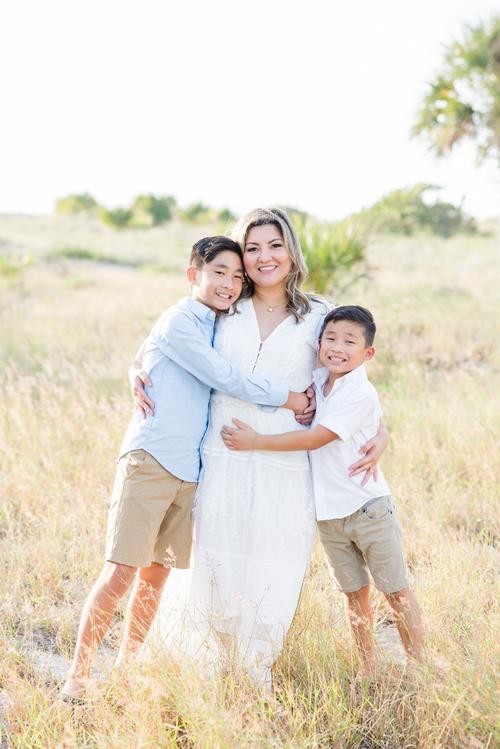 Two boys hug their mother in a yellow field outside on a beach by Jommy Photography. mother and sons #JommyPhotography #JommyFamilies #FloridaFamilyPhotography #Familyphotographers #professionalphotographers #familyportraits