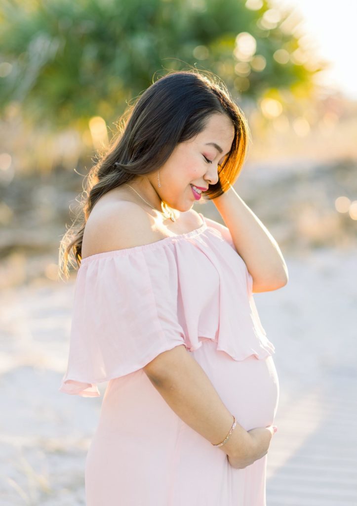 A woman in a pink gown holds her baby bump with the sunshine behind her by Jommy Photography. maternity portraits #JommyPhotography #JommyFamilies #FloridaFamilyPhotography #Familyphotographers #professionalphotographers #familyportraits