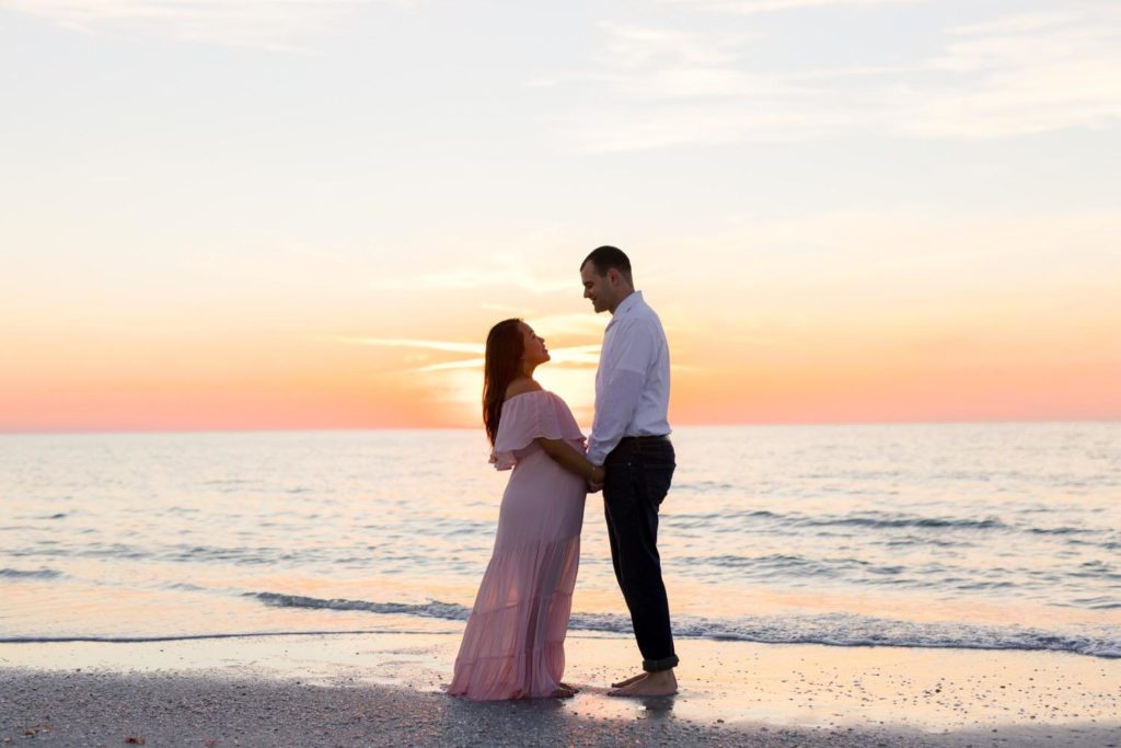 On an FL beach with the sunset behind them parents looking lovingly at one another by Jommy Photography. sunset beach #JommyPhotography #JommyFamilies #FloridaFamilyPhotography #Familyphotographers #professionalphotographers #familyportraits